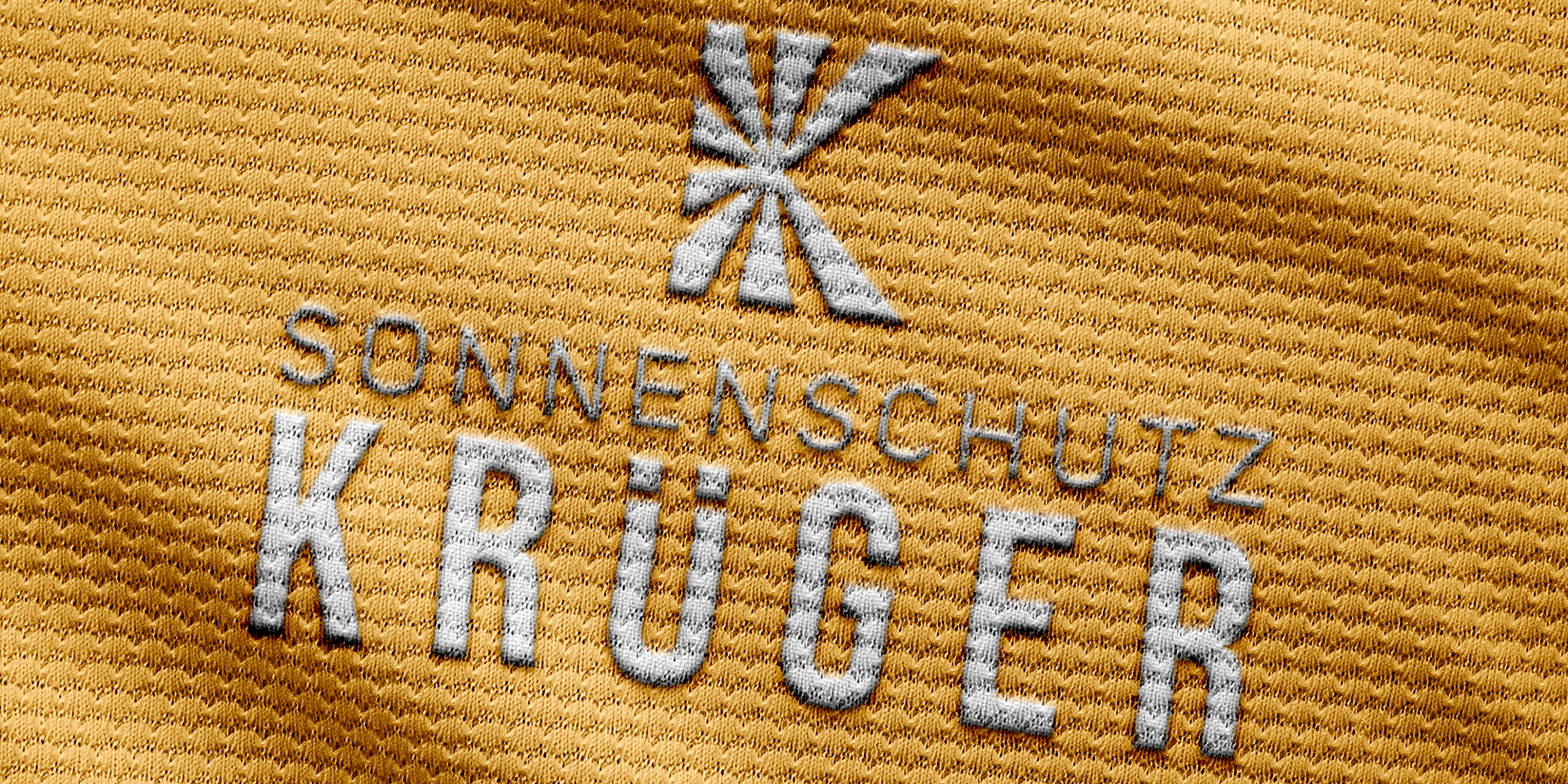 Das Logo der Firma Sonnenschutz Krueger auf einem gelben Stoffuntergrund, detaillieret Ansicht der Fasern und Praegung des Stoffes.