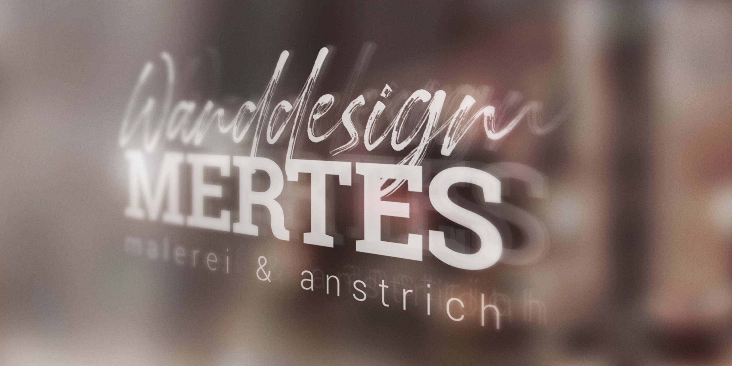 Das Logo der Firma Wanddesign Mertes auf Glas. Unscharfer Hintergrund.