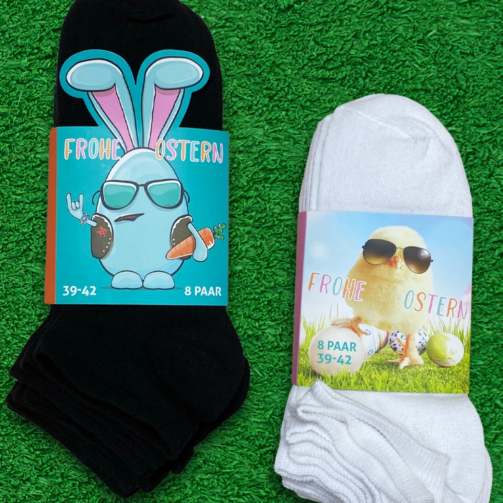 Produktfotografie von zwei verpackten Sneakersocken mit österlichen Motiven. Türkis mit Ei udn Hasenohren und Bunt mit Küken das eine Sonnenbrille trägt. Frophe Ostern als Aufschrift.