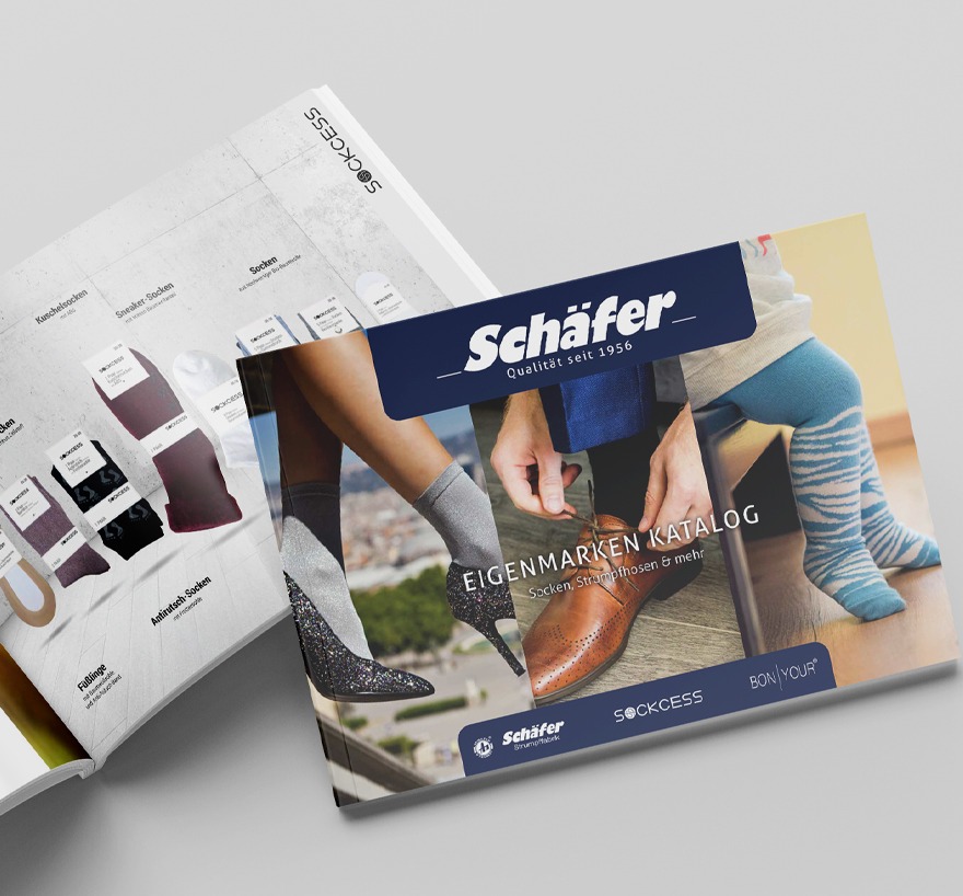 Aufgeschlagenes Magazin im Querformat des Eigenmarkenkataloges der Strumpffabrik Schaefer mit einer Titelseite die glitzernde damenstruempfe zeigt, Herrenschuhe und Socken sowei die Beine eine Babys in einer blaugemusterten Baumwollstrumpfhose. Zu sehen ist ausserdem eine Doppelseite des Mit Socken in hellen Verpackungen vor einem Studiohintergrund. Liegend auf einem hellen Untergrund.