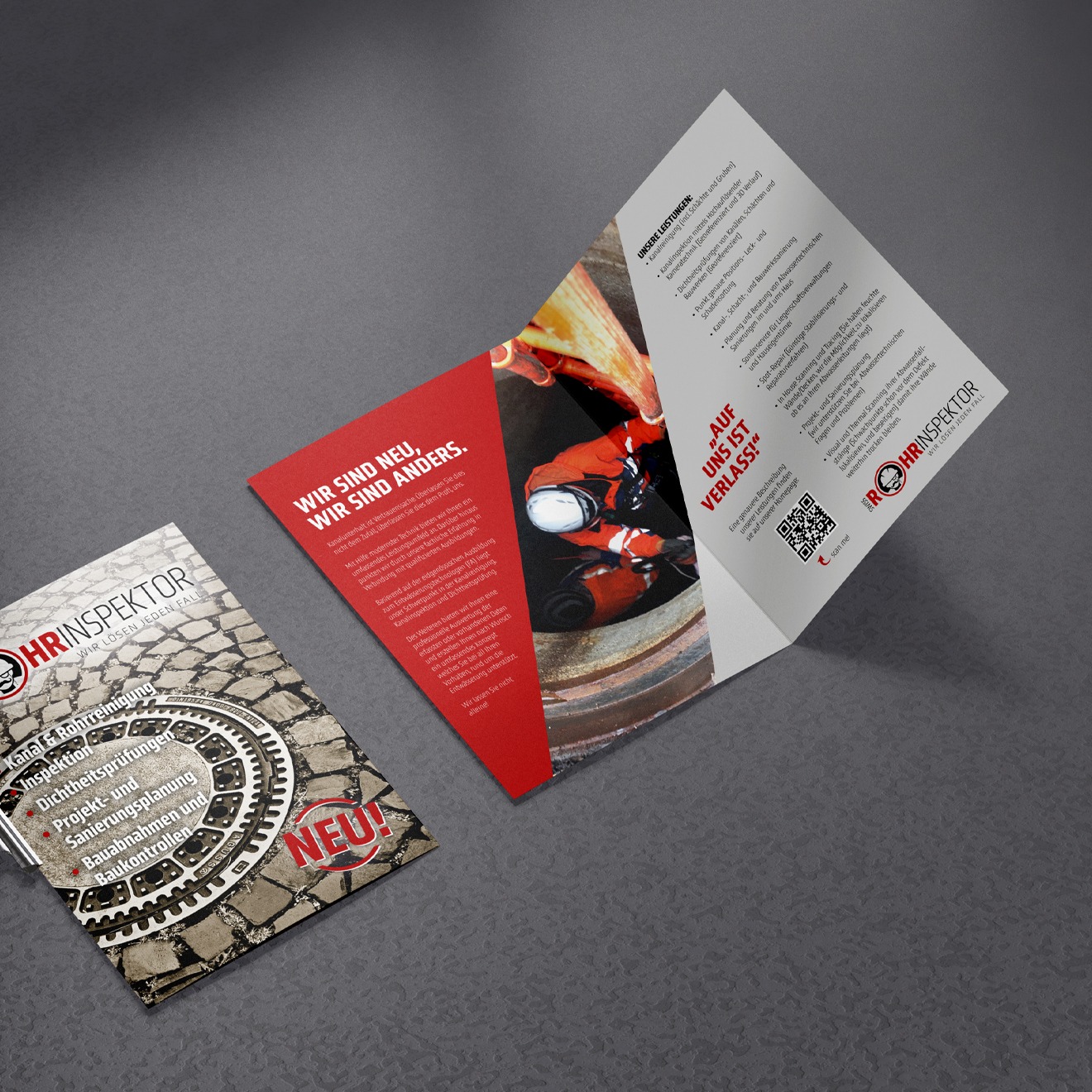 Aufgeklappter Werbeflyer der Firma swiss Rohrinspektor auf dunkelgrauem Lederuntergrund. In den Hauptfarben Rot/weiß/schwarz und grau. Auf der Frontseite des abgebildeteten Flyers ist ein Gullideckel zu sehen. Im Inneren Teil rechts daneben stellt die Firma sich vor.